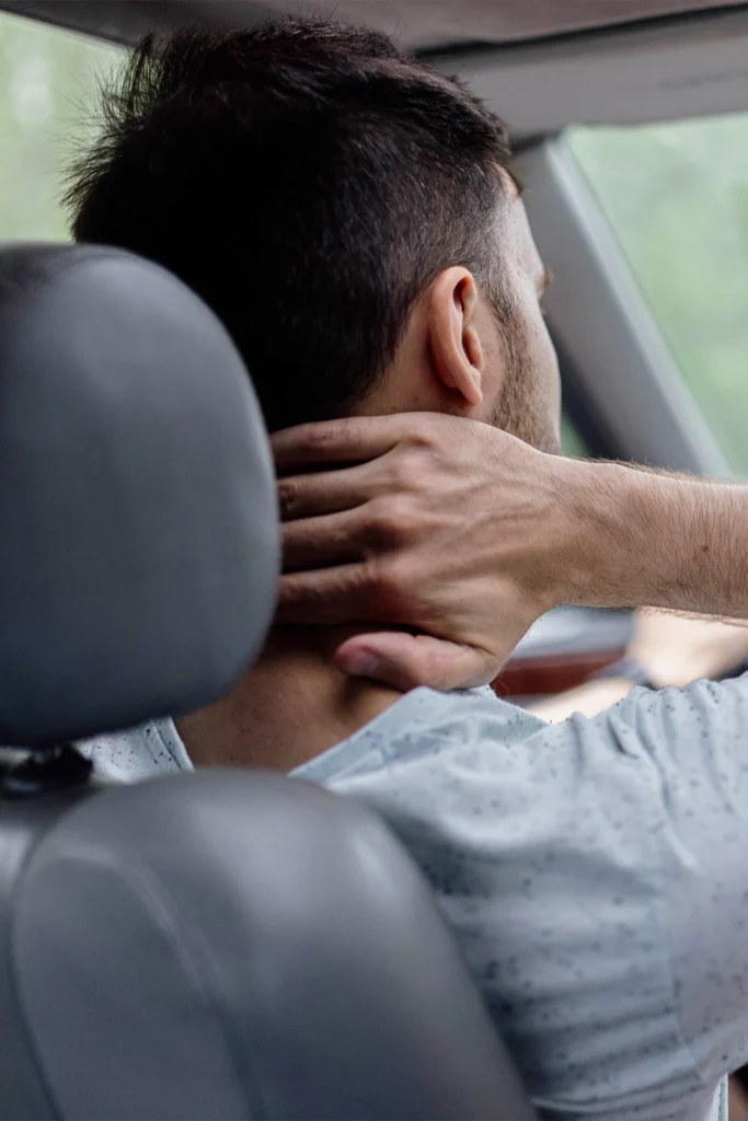 a man driving a car holds the back of his neck