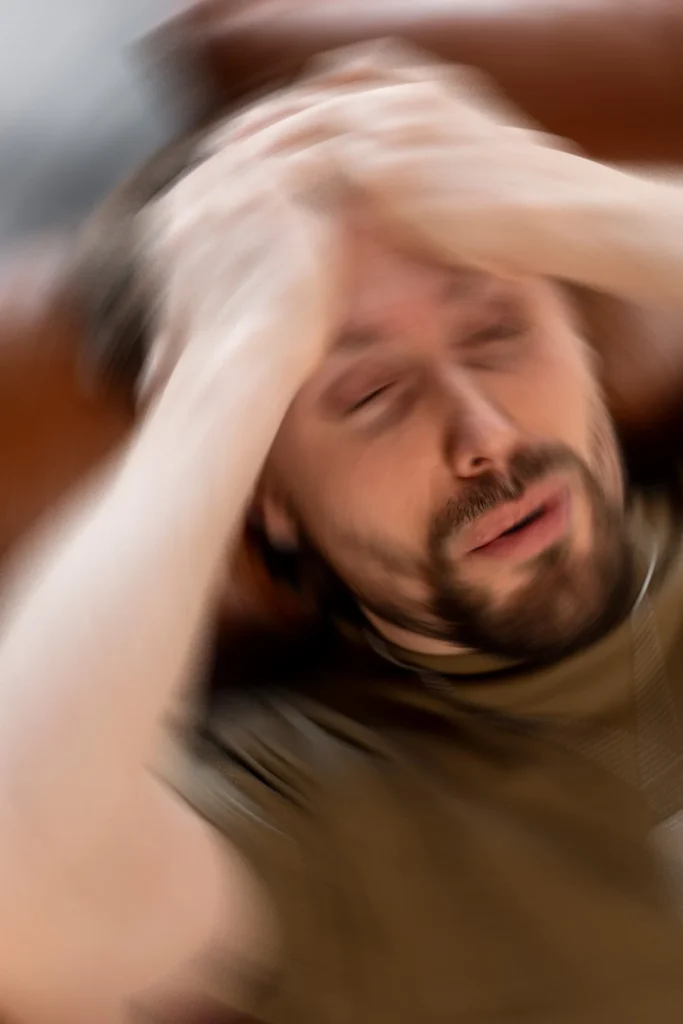 Man Holds His Head As The Room Spins Around Him